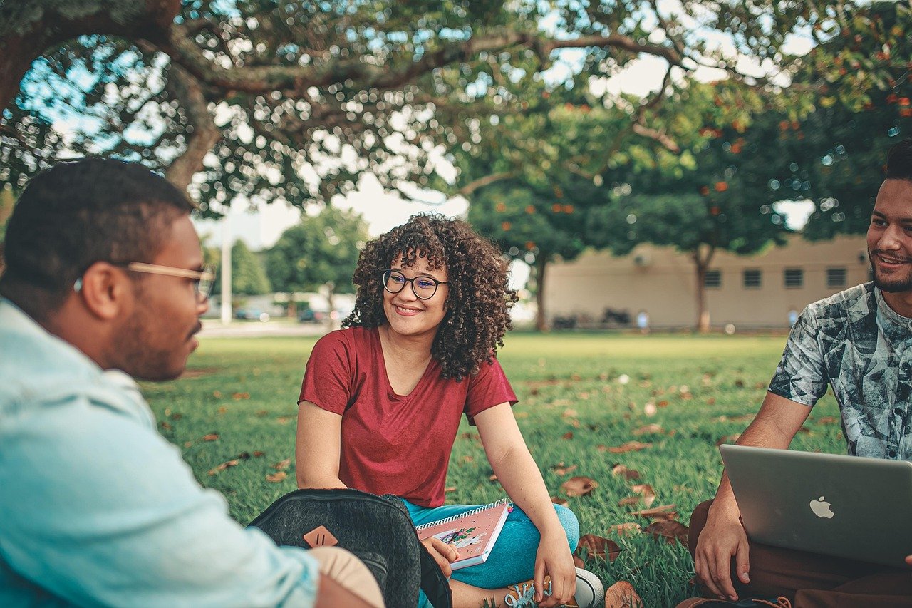 Group of students sitting together on a university campus lawn with a laptop and notebooks